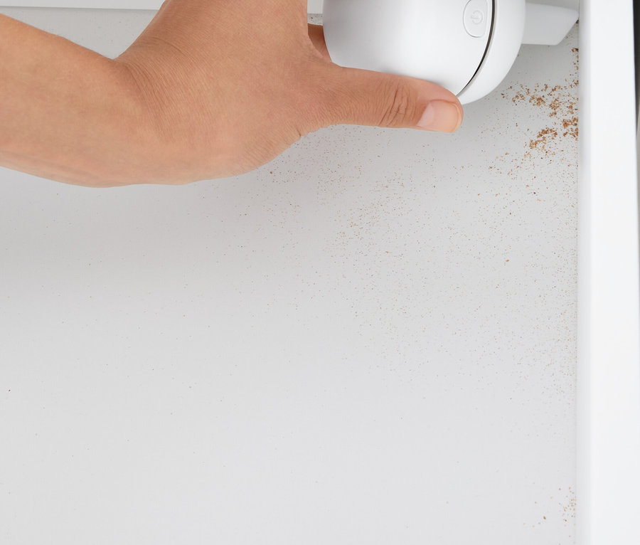 Eine Hand hält einen weißen, kugelförmigen Reiniger in einem weißen Schrank.