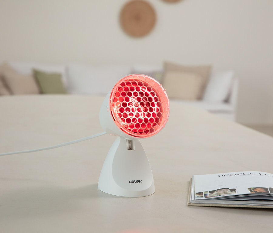 Eine Infrarotlampe von Beurer steht auf einem Tisch neben einem geöffneten Buch.