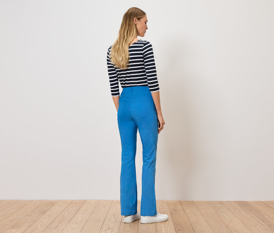 Frau steht mit dem Rücken zum Betrachter, trägt blaue Hosen und ein gestreiftes Shirt.