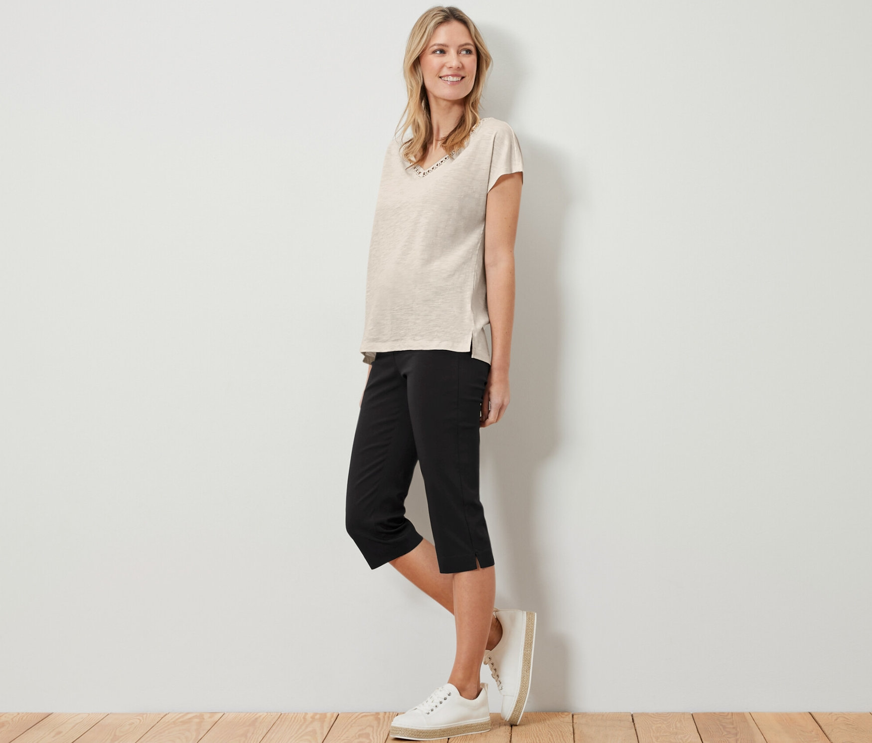 Frau steht und trägt ein beige T-Shirt und eine schwarze 3/4-Stretchhose.