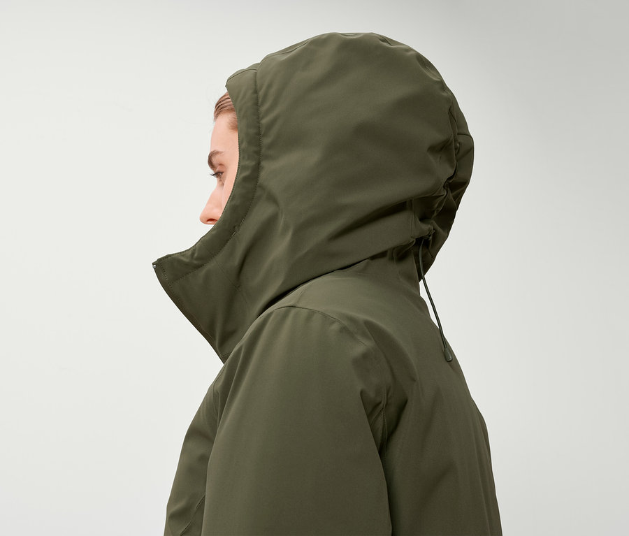 Profil einer Frau, die eine olivgrüne Jacke mit Kapuze trägt.