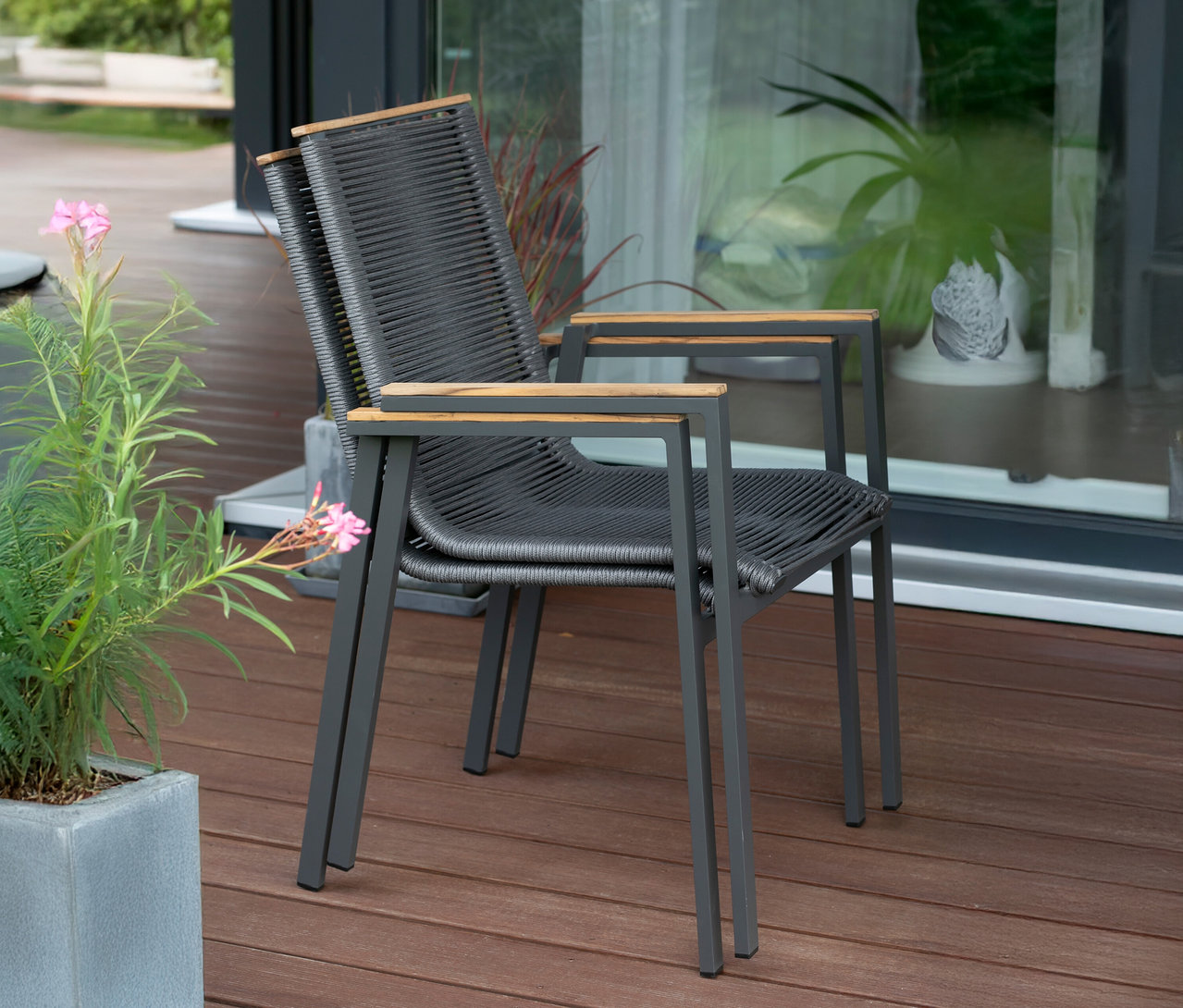 Zwei graue Stühle mit Armlehnen aus Holz stehen auf einer Terrasse.