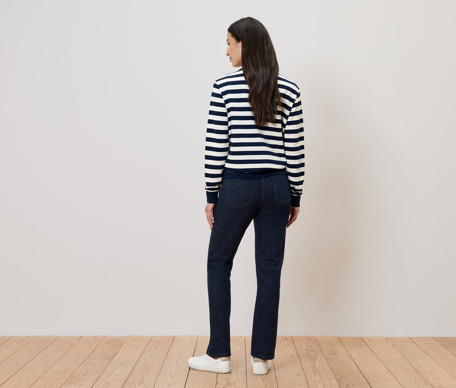 Rückansicht einer Frau mit langen, dunklen Haaren, die einen gestreiften Pullover, Jeans und weiße Schuhe trägt.