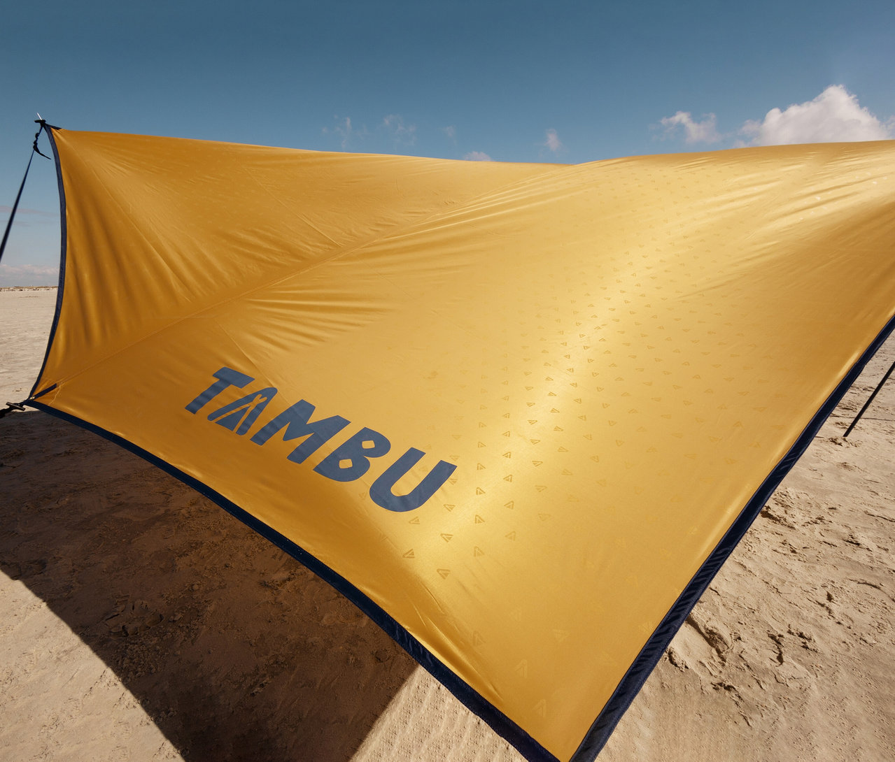 Gelbes Tambu »PALA« Tarp/Sonnensegel auf Sand mit blauem Himmel.