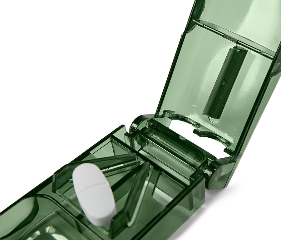 Eine weiße Tablette liegt in einem offenen, grünen Tablettenteiler.