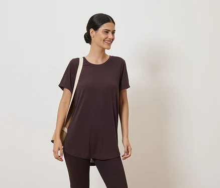 Frau mit Dutt trägt braunes T-Shirt und Leggings. Über der Schulter hängt eine beige Stofftasche.