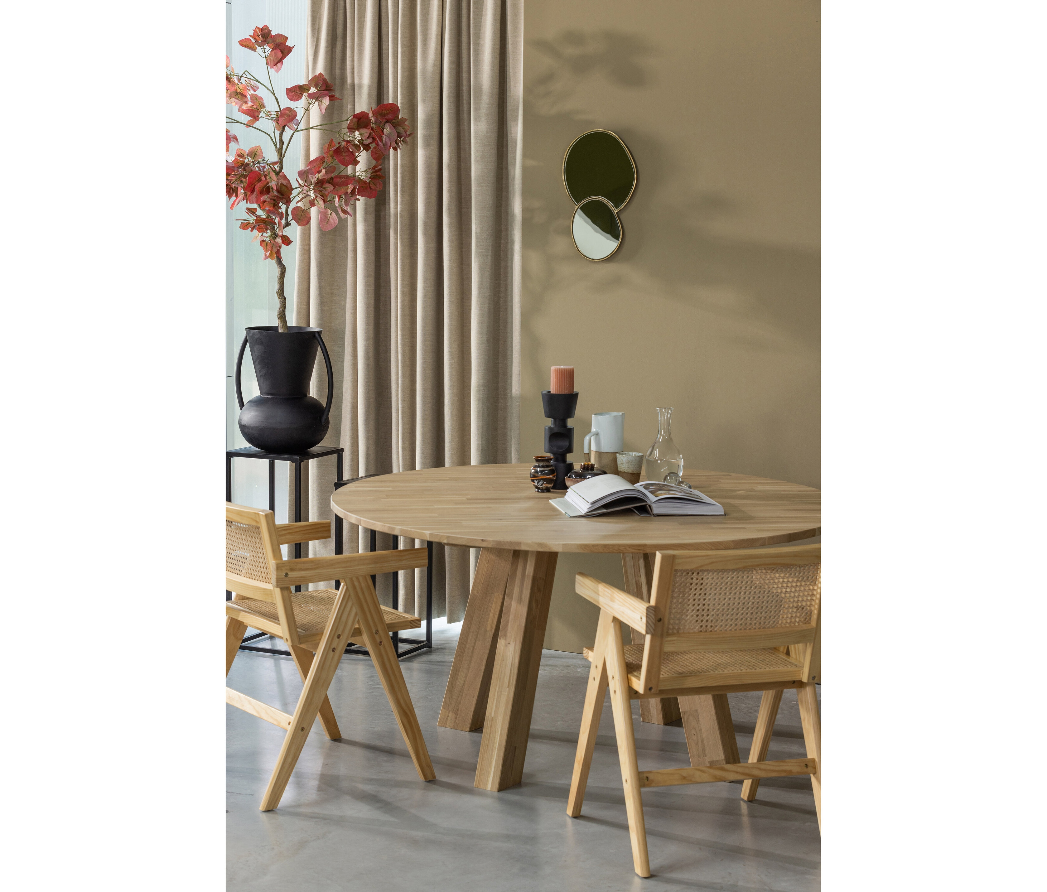Zwei Holzstühle stehen am runden WOOOD »Rhonda« Esstisch (ca. 150 cm). Auf dem Tisch liegen Dekoartikel und ein Buch.
