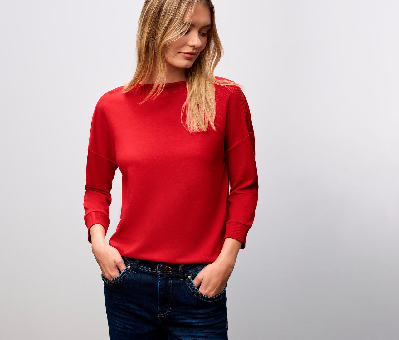 Frau mit blonden Haaren trägt ein rotes Street One T-Shirt mit Rippdetail und Jeans.