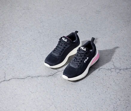 Zwei schwarze Fila-Sneakers stehen auf einem grauen Betonboden.