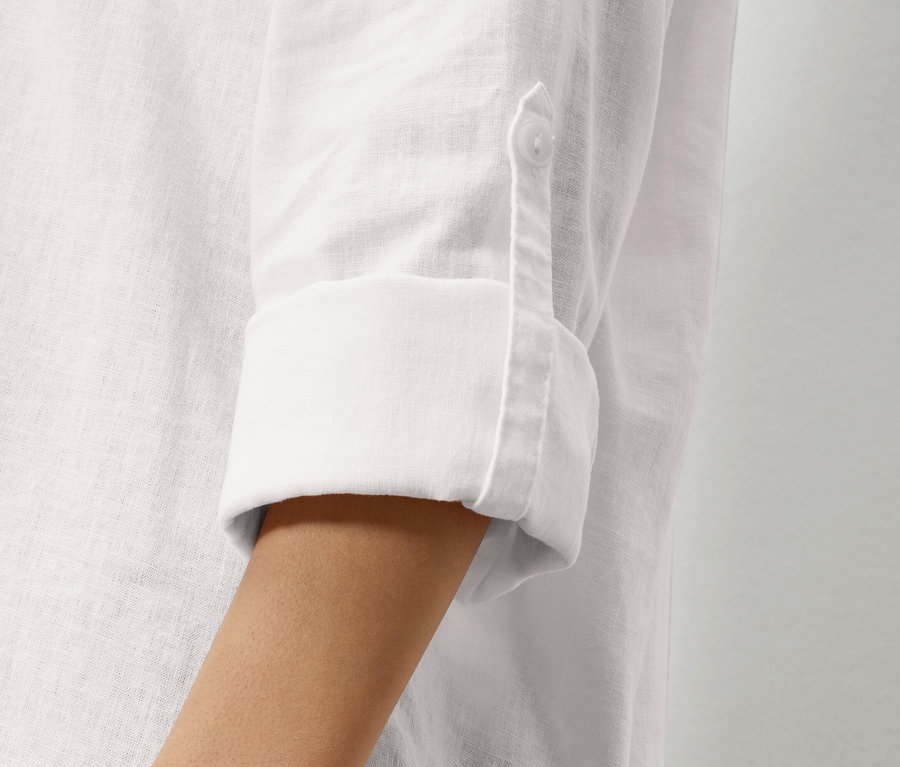 Detailansicht eines Ärmels eines weißen Leinenhemdes mit hochgekrempeltem Ärmel und einem Knopf.