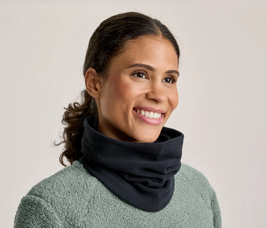 Eine lächelnde Frau mit dunklem, zurückgebundenem Haar trägt einen schwarzen Halswärmer und ein mintgrünes Fleece-Oberteil. Sie blickt nach rechts.