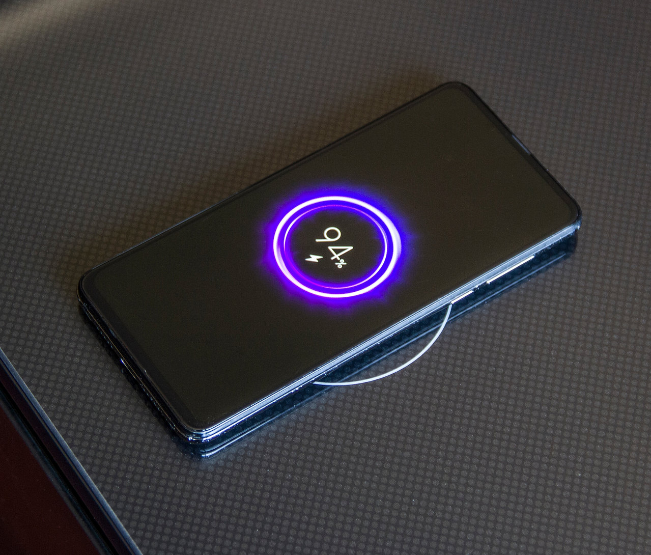 Schwarzes Smartphone lädt kabellos auf dunkler Oberfläche.