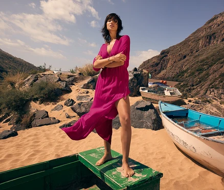 Frau steht barfuß auf einem Boot am Strand und trägt ein Triumph Beach MyWear Kaftan Maxi Dress.