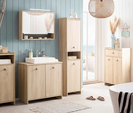 Badezimmer mit Waschtisch, Spiegelschrank, Hochschrank und Kommode in hellem Holz. Dekorationen im maritimen Stil und Badewanne im Vordergrund.