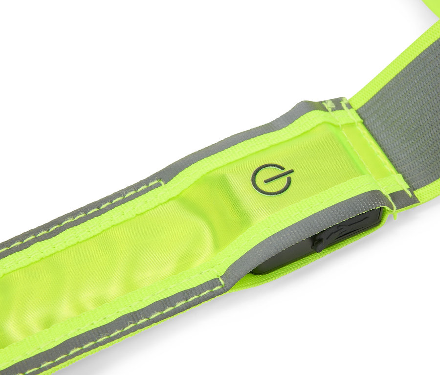 Nahaufnahme eines neongelben Reflexbandes mit grauen Reflexstreifen, einem Einschaltsymbol und einer dunklen Steuereinheit.
