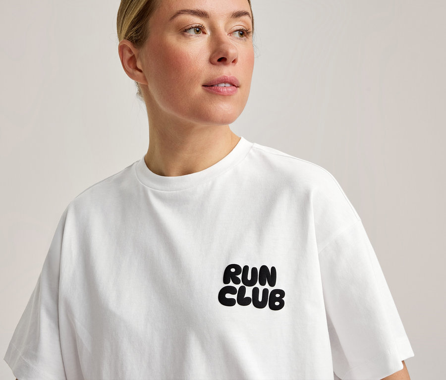 Eine Frau trägt ein weißes Sportshirt mit dem Aufdruck „RUN CLUB“ auf der Brust.