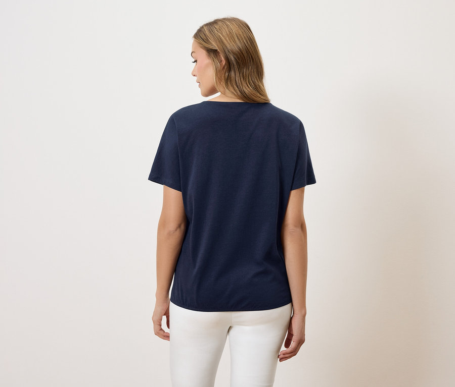 Eine Frau mit blonden Haaren trägt ein marineblaues T-Shirt und weiße Hosen.