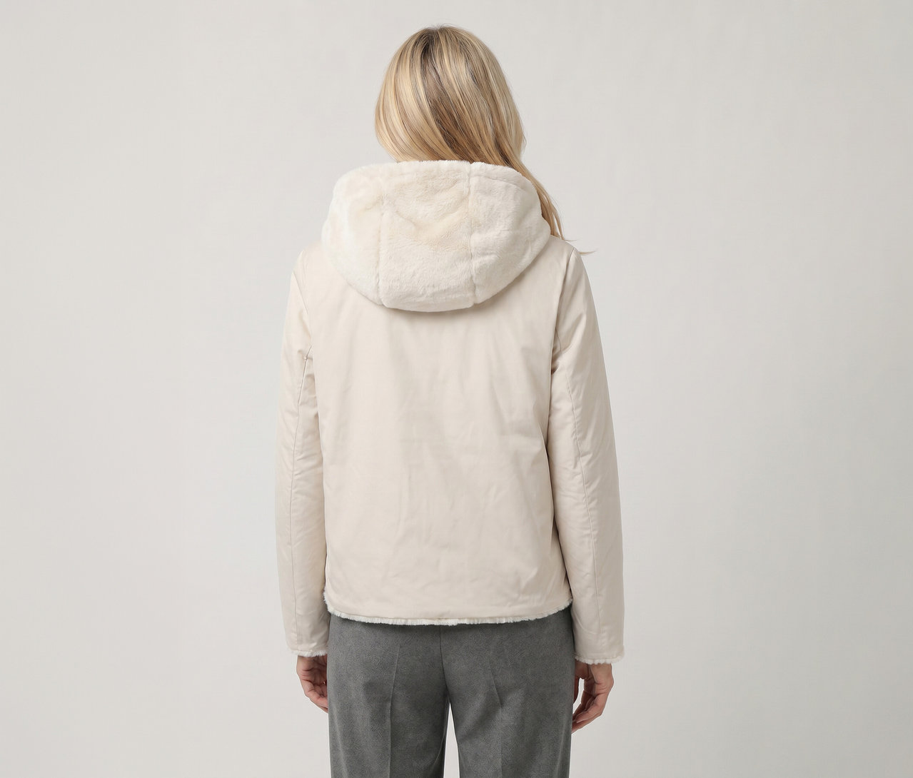 Blonde Person von hinten, trägt eine hellbeige Jacke mit Kapuze mit Kunstfellfutter und graue Hose.