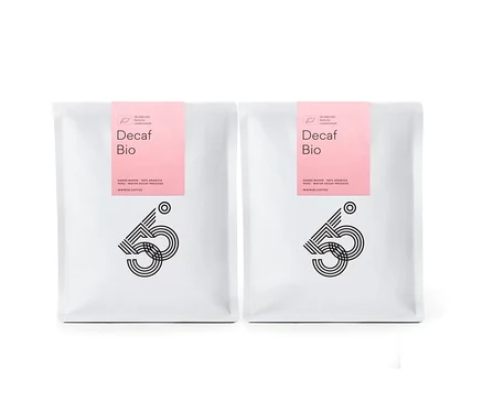 Zwei weiße Tüten Decaf Bio Kaffee mit rosa Etikett stehen nebeneinander vor einem weißen Hintergrund.