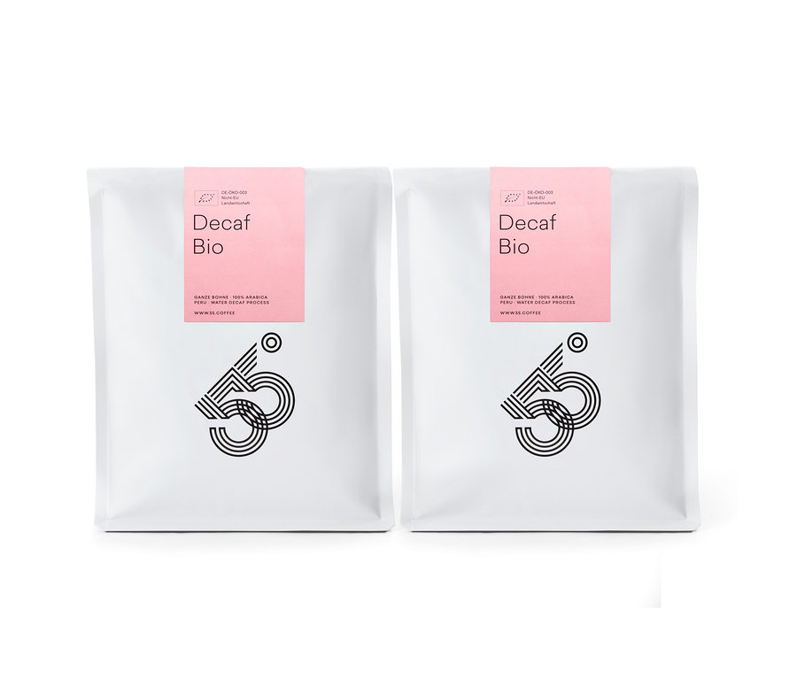 Zwei weiße Tüten Decaf Bio Kaffee mit rosa Etikett stehen nebeneinander vor einem weißen Hintergrund.