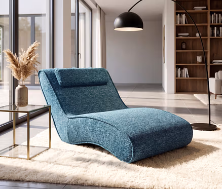 Ein modernes Wohnzimmer mit einer blauen Chaiselongue auf einem flauschigen weißen Teppich. Daneben steht ein Beistelltisch aus Glas und Gold mit Pampasgras in einer Vase. Eine schwarze Bogenstehlampe und große Fenster sind im Hintergrund zu sehen.