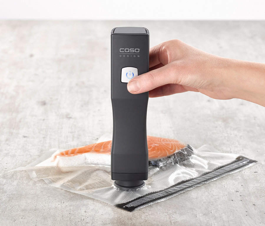 Hand drückt den Knopf des schwarzen CASO Vacu OneTouch Handvakuumierers über einem Vakuumbeutel mit Lachs.