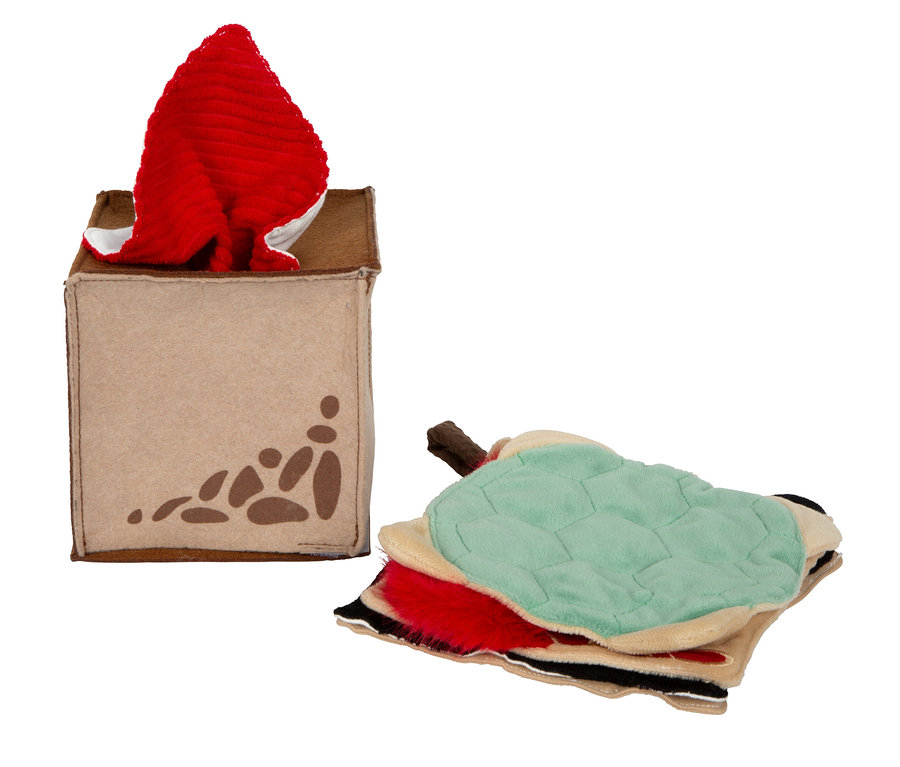 Beige Stoffbox mit braunen Pfotenabdrücken, aus der ein rotes Stoffstück ragt, daneben ein Stapel bunter Stoffstücke, darunter ein hellgrünes mit Schildkrötenpanzer-Textur.