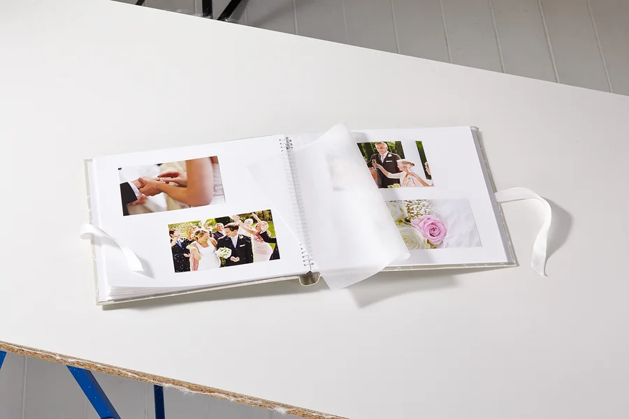 Geöffnetes Hochzeitsalbum mit Fotos auf einem weißen Tisch.