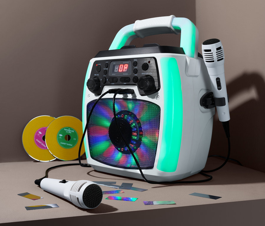 Ein weißes Karaoke-Set mit zwei Mikrofonen, zwei CDs und Konfetti auf einem Tisch.