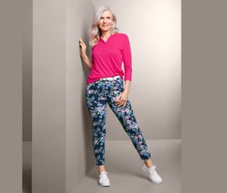 Frau, die sich an eine Wand lehnt, trägt ein pinkfarbenes Oberteil und eine bedruckte Bengalin-Hose.