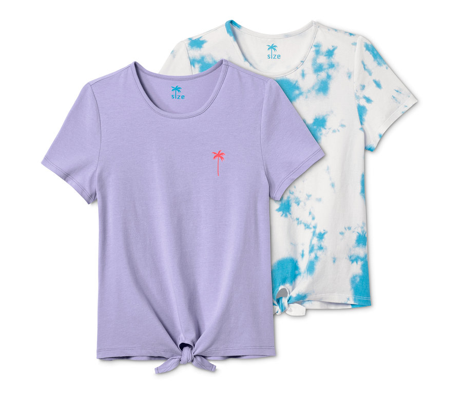 Zwei Knoten-Shirts liegen nebeneinander, eines lila mit Palmenbild, das andere weiß mit blauem Batikmuster.