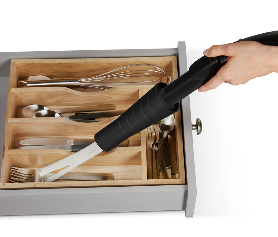 Hand mit Staubsaugeraufsatz reinigt Schublade mit Besteck.