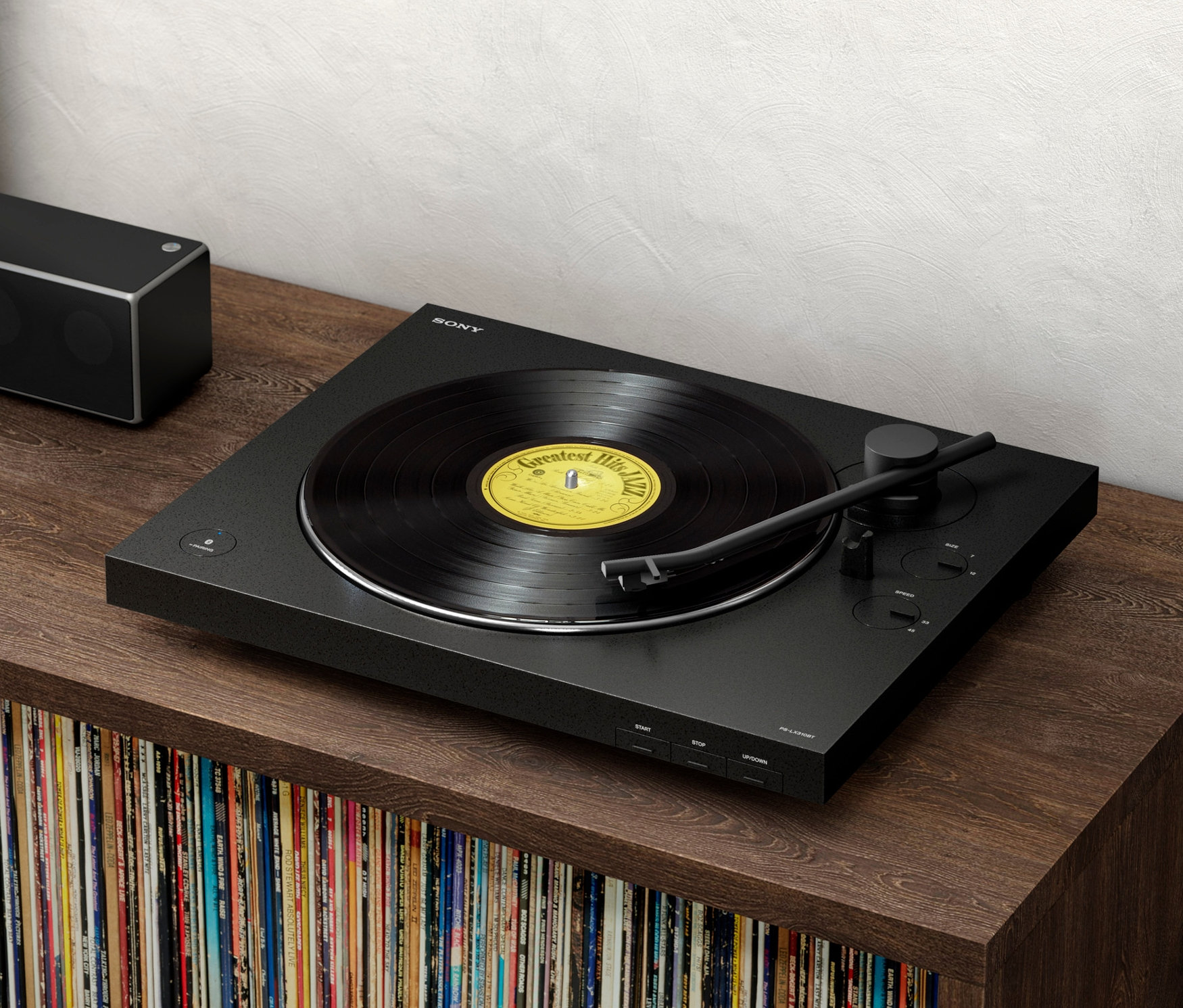 Schwarzer Plattenspieler mit Schallplatte auf einem braunen Holzschrank, daneben ein schwarzer Lautsprecher. Zu sehen ist ein Sony-Plattenspieler »PS-LX310BT«.