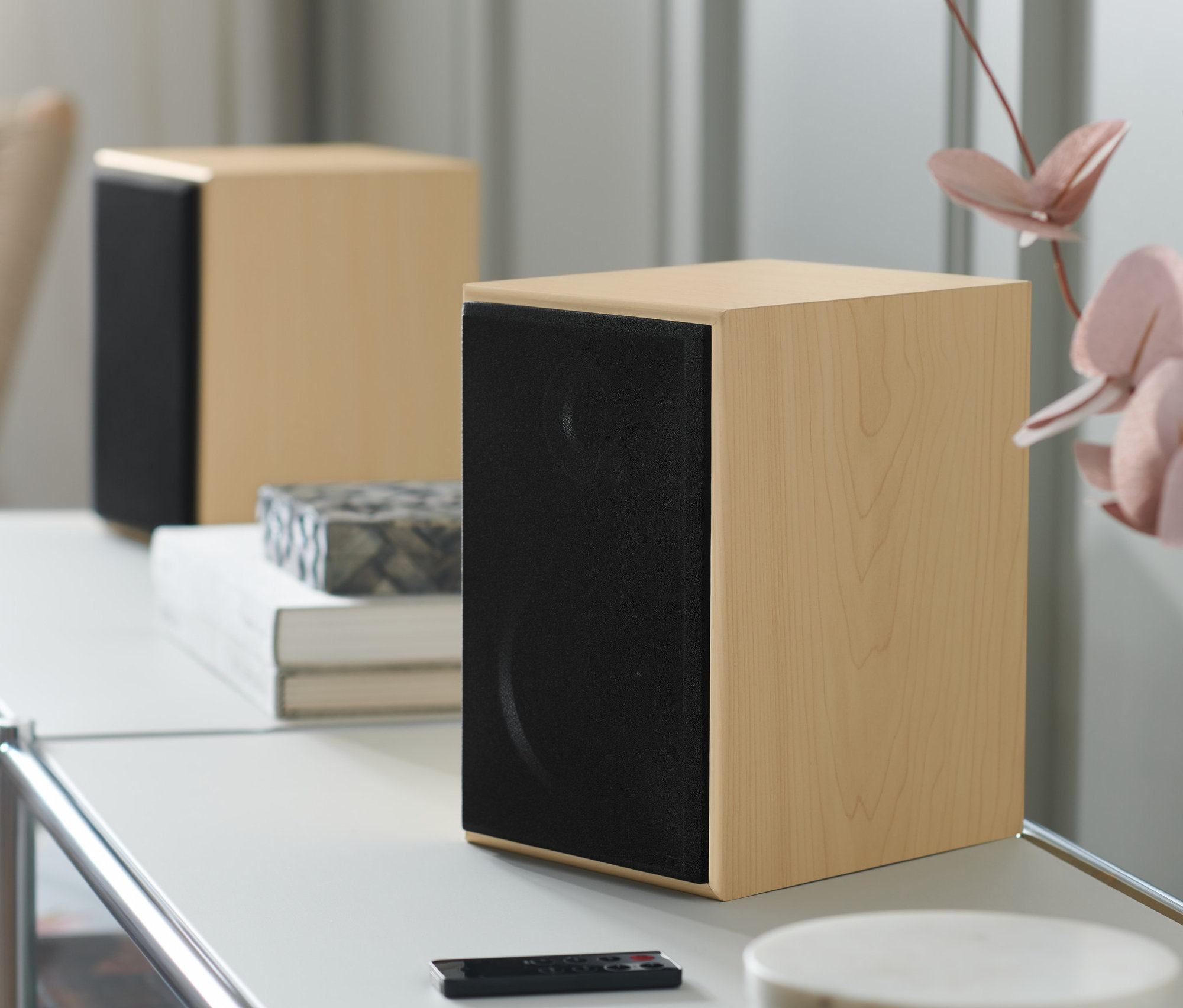 Zwei Stereo Regallautsprecher mit Bluetooth® auf einem weißen Tisch mit einer Fernbedienung.