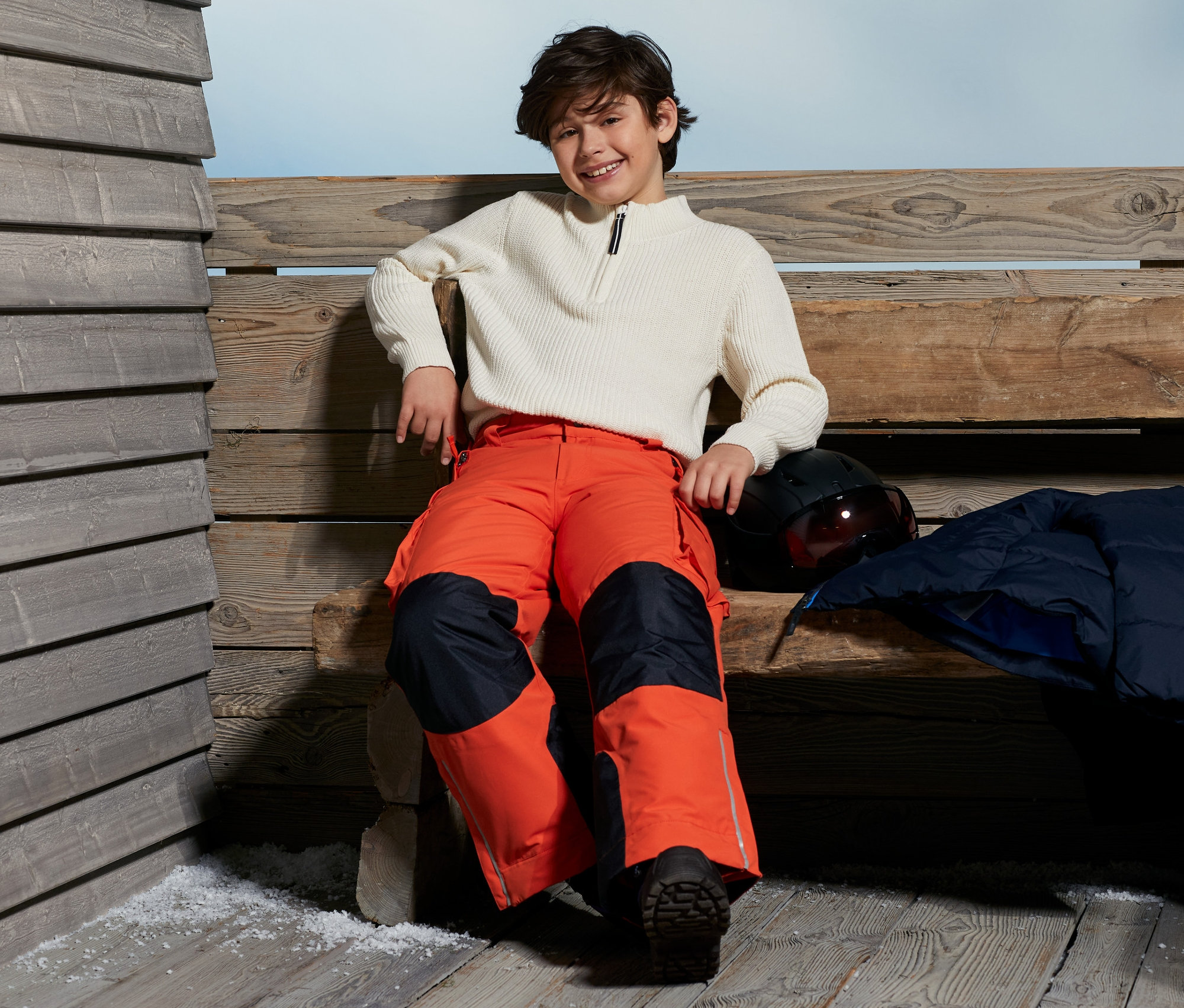 Ein Junge sitzt auf einer Bank und trägt eine Snowboardhose.