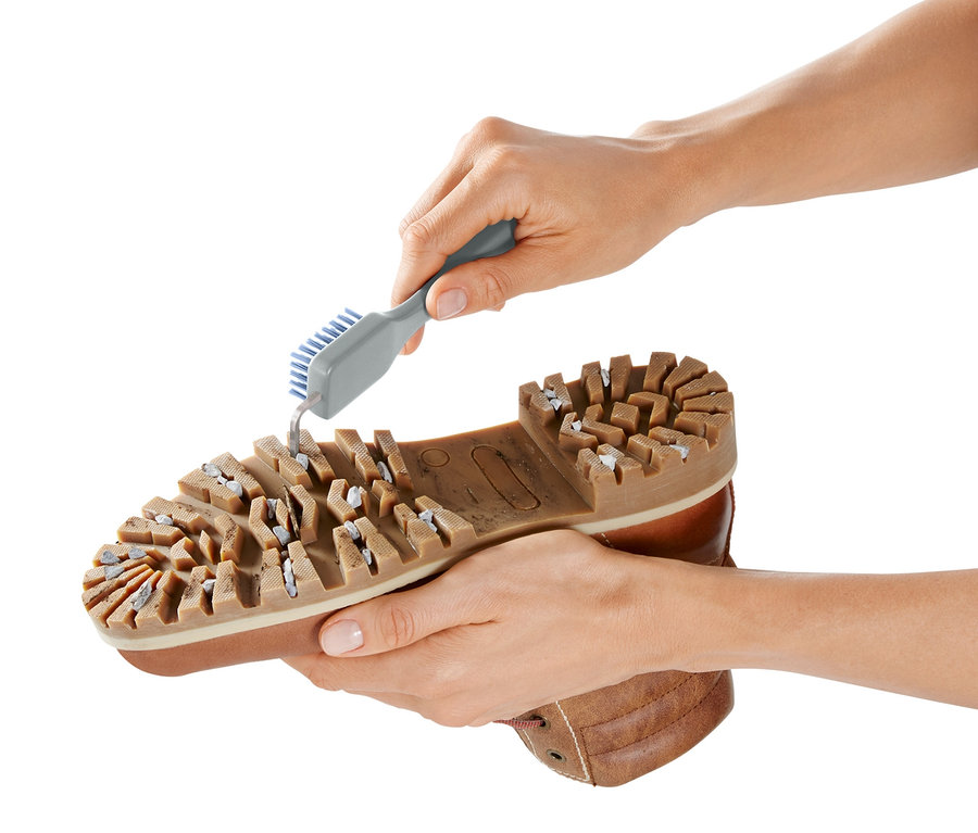Hände reinigen die Sohle eines braunen Schuhs mit einer Schuhsohlen-Reinigungsbürste.