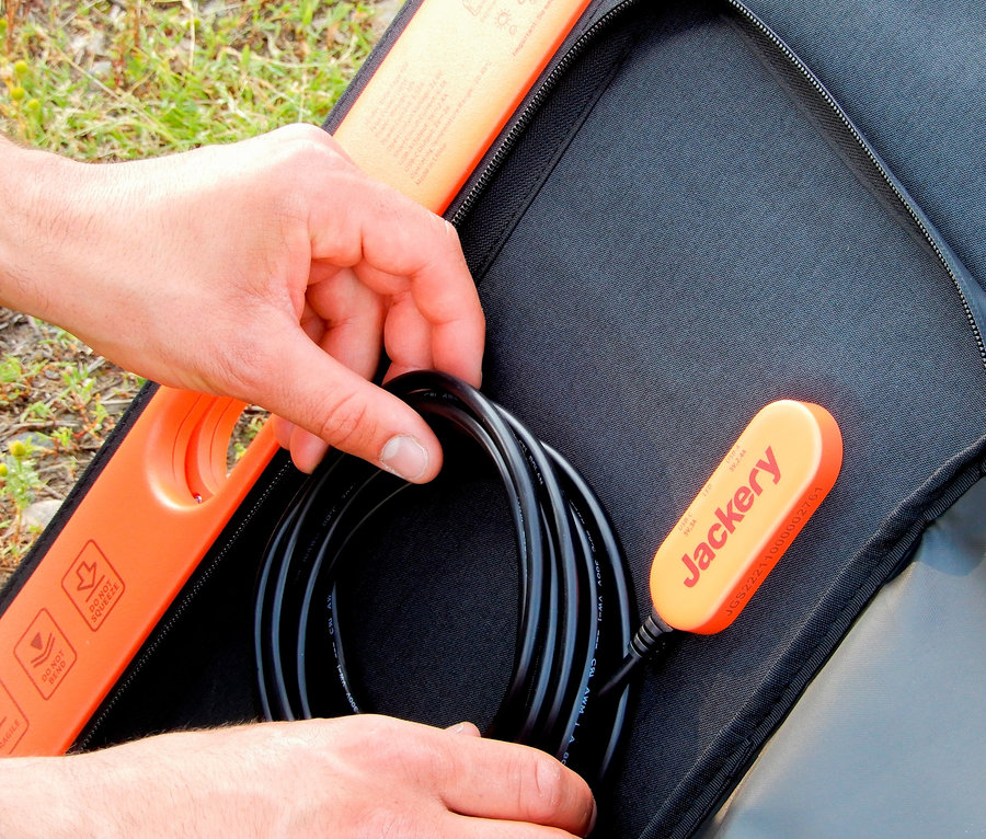 Eine Hand verstaut ein schwarzes Kabel in einer Tasche neben einem orangefarbenen Jackery-Anschluss.