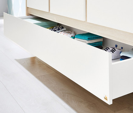 Offene Schublade einer weißen Kommode mit diversen Artikeln darin.