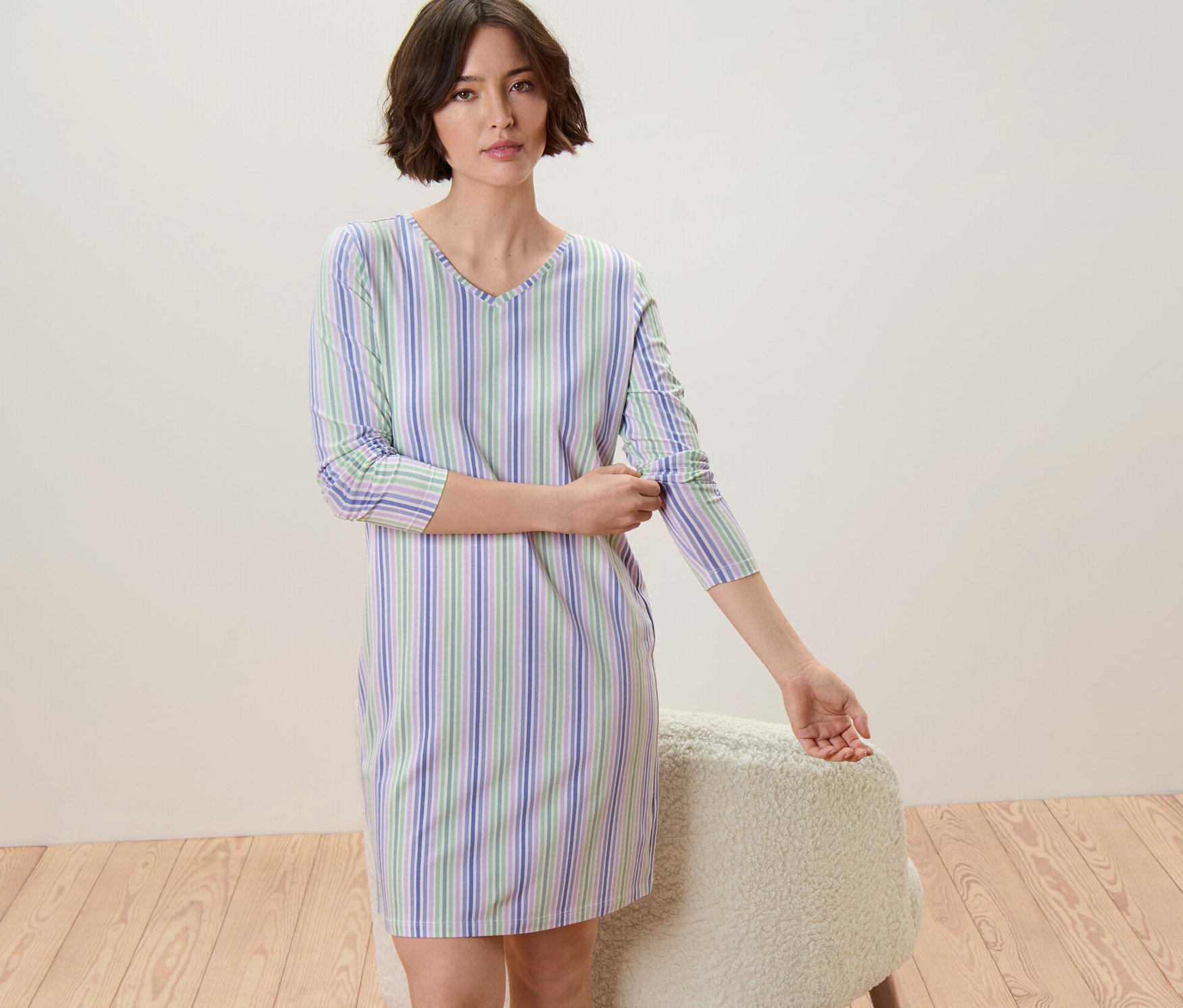Frau krempelt die Ärmel eines blau, grün und weiß gestreiften Nachthemds hoch.