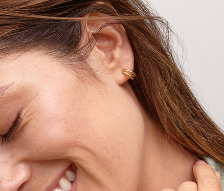 Lächelnde Frau trägt einen Gold Ring V Zirkonia und Gold-Doppelcreolen.