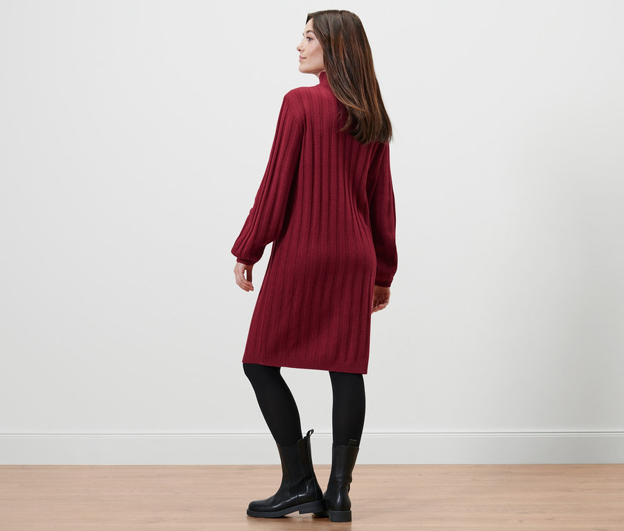 Frau posiert in geripptem Strickkleid mit Stehkragen, schwarzen Leggings und schwarzen Stiefeln.