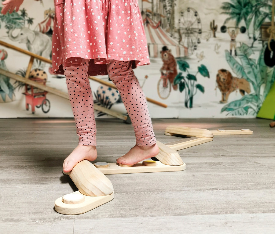 Ein Mädchen in einem rosa Kleid und Leggings mit Punkten balanciert barfuß auf den small foot Balancierstegen »Adventure«.