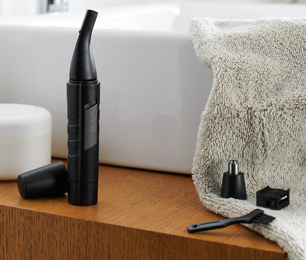 Ein Nasen- und Ohrhaar-Trimmer steht mit Zubehör auf einem Holzregal im Badezimmer.