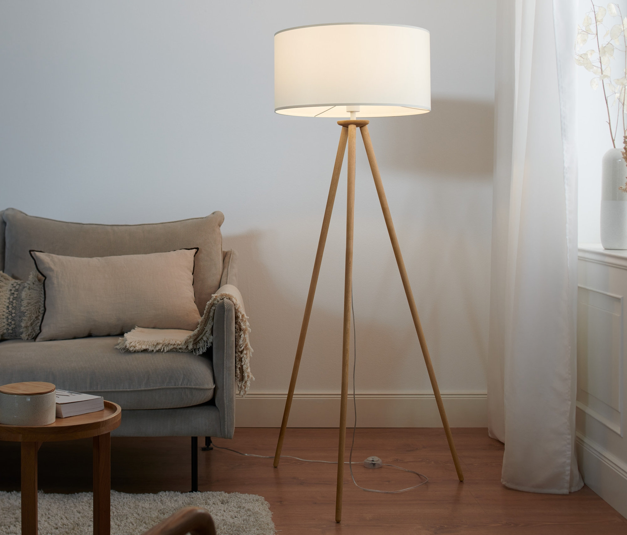 Wohnzimmer mit Sofa und Dreibein Stehleuchte aus Holz.