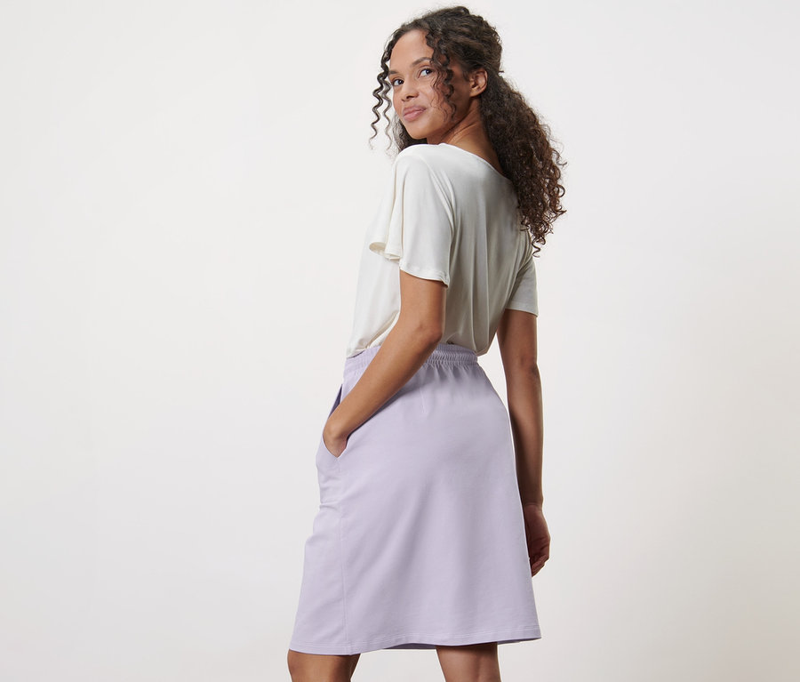 Frau posiert und hat Hände in den Taschen von fliederfarbenem Sweatrock.