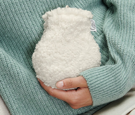 Person im Pullover hält eine Mini-Wärmflasche.