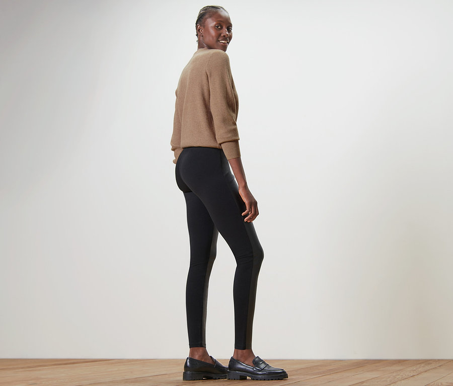 Frau posiert in Leggings im Materialmix und Pullover.