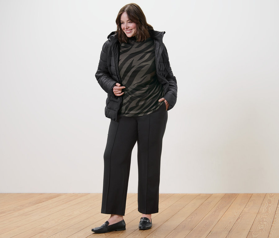 Frau posiert in Steppjacke mit Kapuze, bedrucktem Mesh-Rollkragenshirt und Jerseyhose mit Biese.