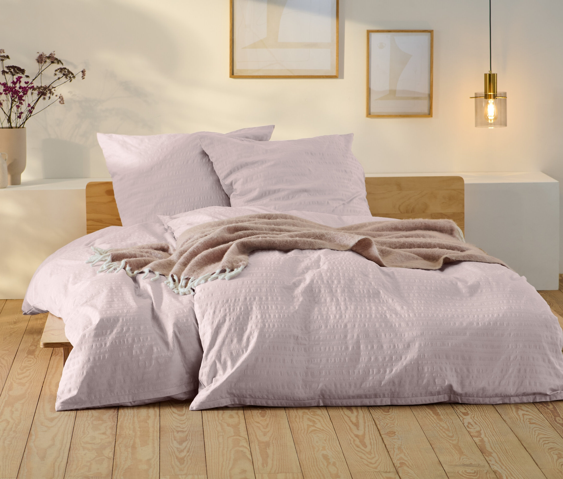 Rosafarbene Seersucker-Bettwäsche in Normalgröße und Übergröße auf einem Bett mit Holzrahmen.