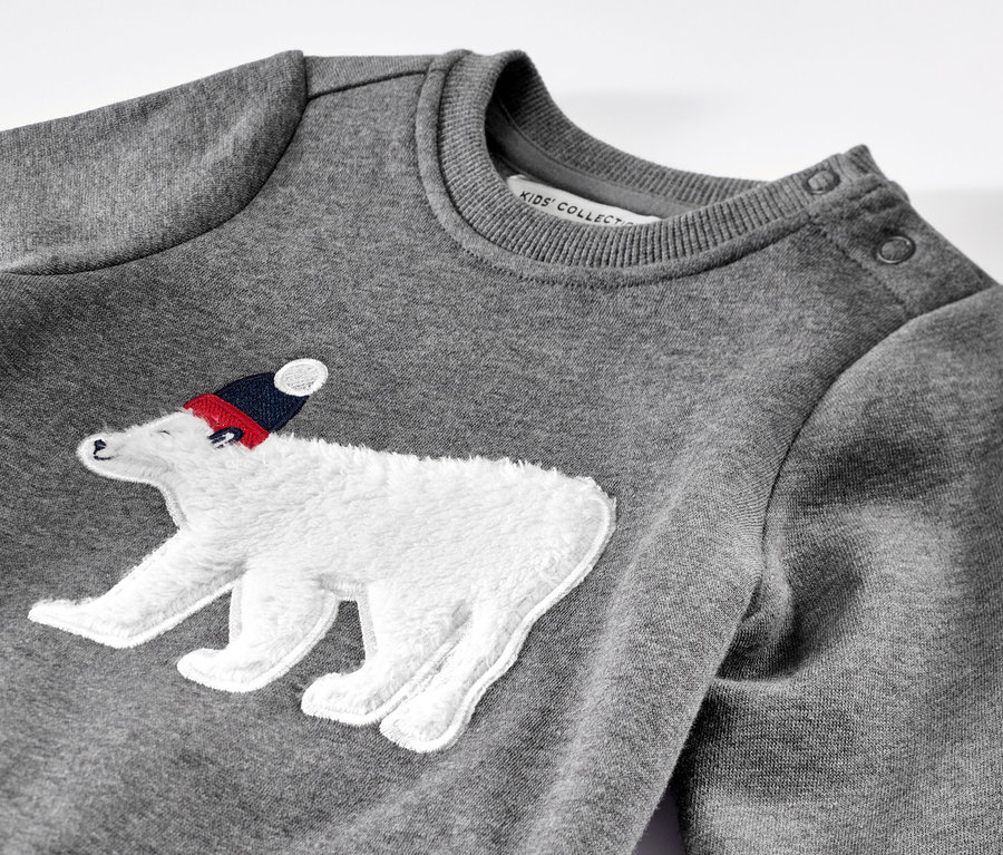 Detailansicht eines grauen Kinder-Sweaters mit einem aufgenähten Eisbären mit Mütze.